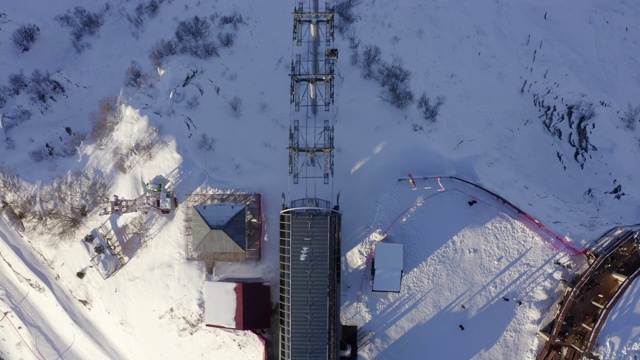 雪山冬季滑雪场的滑雪缆车，供滑雪者和滑雪板者鸟瞰图。俯视图从飞行的无人机滑雪电梯在冬季雪坡工作。白雪皑皑的山区度假胜地视频素材