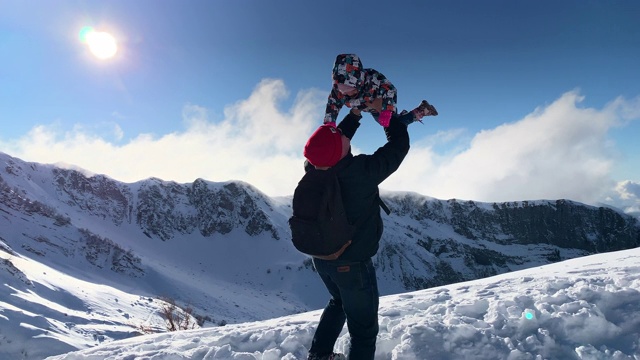 快乐的父亲把小女儿抛在雪山景观的背景上。爱玩的爸爸在冬天散步时把有趣的孩子吐出来。冬季活动，快乐休闲视频素材