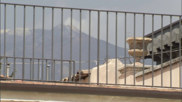 远处的一座火山在屋顶露台的围栏后面升起浓烟。视频素材