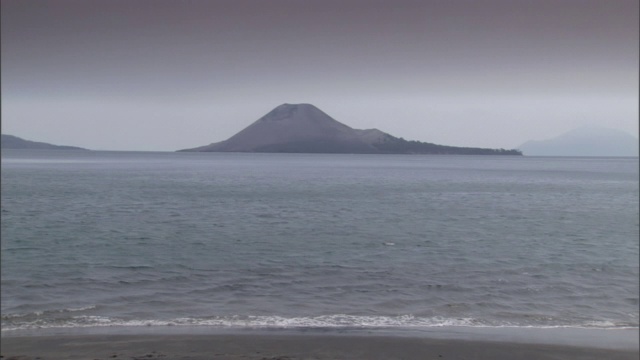 海浪轻轻地冲上岸在一个火山的前景。视频素材