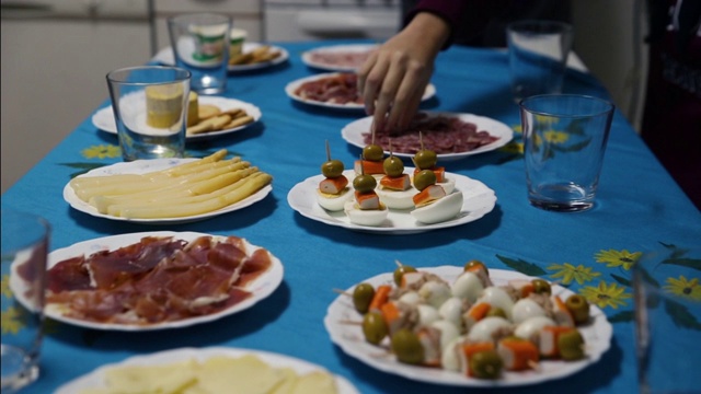 餐桌上摆满了开胃菜，有塞拉诺火腿、奶酪、芦笋和鸡蛋串，还有一只手伸出来准备吃馅饼视频素材