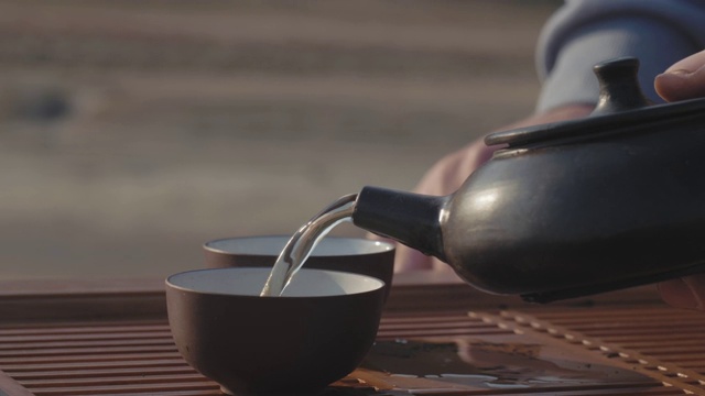 一个男性的手从一个粘土茶壶倒茶从宜兴到碗的特写。手工制作的泥茶壶。中国茶道。4 k的视频。23.98帧/秒视频素材