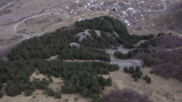 鸟瞰山间蜿蜒的汽车道路。无人机俯瞰山谷中的城市建筑。汽车在蜿蜒的山路上行驶视频素材