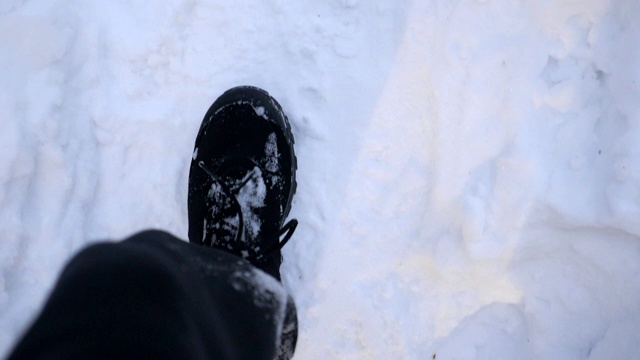 在雪道上行走的男性脚的细节视图。穿着靴子的人走在路上，踩在洁白的雪地上。难以辨认的徒步旅行者在森林中漫步。冬天的概念。POV慢动作近距离俯视图视频素材