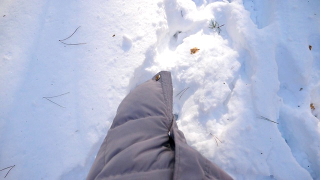 俯视图女人的腿踏在深雪和踢它。在寒冷的冬日里，一个面目全非的徒步旅行者穿过白雪覆盖的森林。女孩去户外。POV慢动作特写视频素材