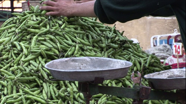 在一个户外市场上，一名小贩正在把菜豆堆在秤旁。视频素材