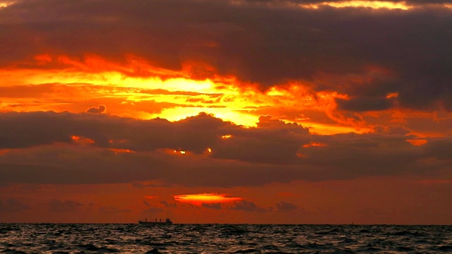 夕阳下，橘黄色的天空和暗红色的云在海上移动，水面的小波浪反射着阳光视频素材