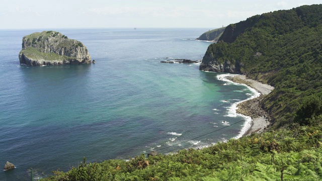 Gaztelugatxe岛在美丽的蓝色海洋和小波浪在西班牙，白天。蔚蓝的天空，蓝色的颜色，云彩，4K超高清，茂密的森林与树木。视频素材