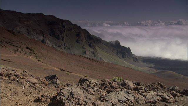 一层云环绕着一个火山口，岩石中间生长着一些灌木。视频素材