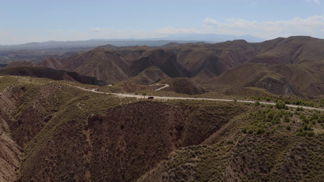 史诗航拍的干燥山谷和山脉Gorafe, Desierto de los Coloraos在蓝天，内华达山脉，格拉纳达，西班牙。在安达卢西亚，有植被的西班牙沙漠峡谷。孤独道路上的汽车4K。视频素材