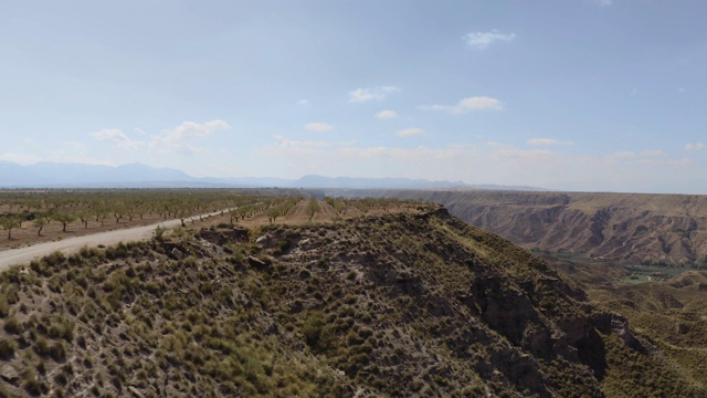 无人机在西班牙格拉纳达内华达山脉的蓝天中拍摄的Gorafe, Desierto de los colorado的干燥山谷和山脉。在安达卢西亚，有植被的西班牙沙漠峡谷。跟踪在树上。视频素材