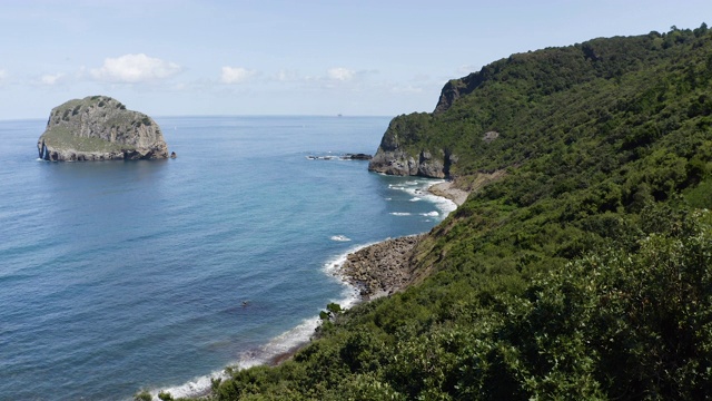 西班牙Gaztelugatxe岛白天的无人机镜头，美丽的蓝色海洋中有小波浪。蔚蓝的天空，蓝色的颜色，云彩，4K超高清，茂密的森林与树木。向上移动。视频素材