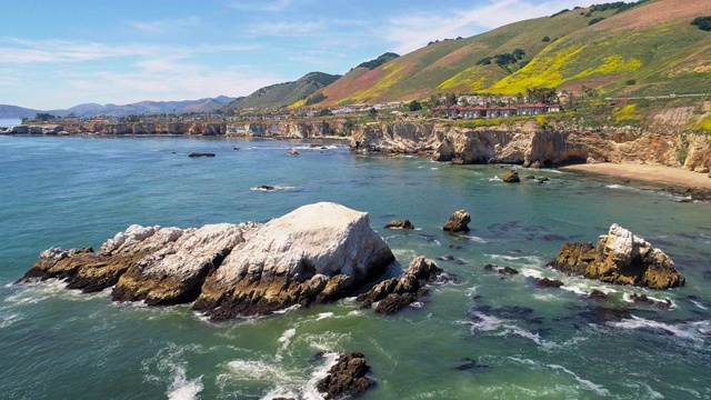 在阳光明媚的春日，加州西海岸太平洋上的小城市Pismo Beach附近的悬崖、岩石和偏远的101公路的海岸线全景鸟瞰。无人机4K超高清视频与向后相机运动视频素材