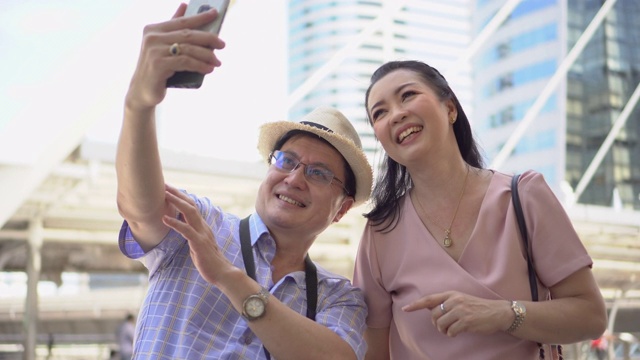 快乐的亚洲老年夫妇游客旅游使用智能手机拍照一起在城市户外城市。老人旅行者的生活方式。老年妇女度假。老龄化社会的概念。视频素材