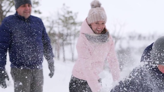 爸爸、妈妈、儿子和小女儿在雪天的树林里玩雪球。友好时尚的家庭在森林里扔雪的乐趣。人们一起享受寒假。慢动作视频素材