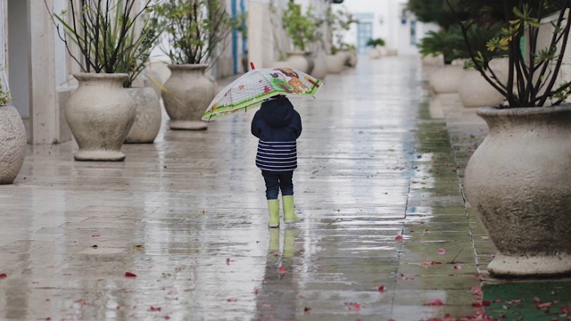 一个穿着胶靴的孩子在雨中拿着喇叭走着视频素材