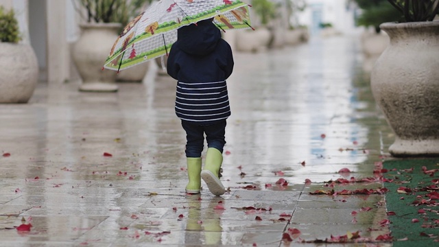 一个穿着胶靴的孩子在雨中拿着喇叭走着视频素材