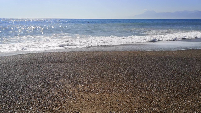 巨大的海浪拍打在沙石沙滩上，大海的背景是山脉- 22视频素材