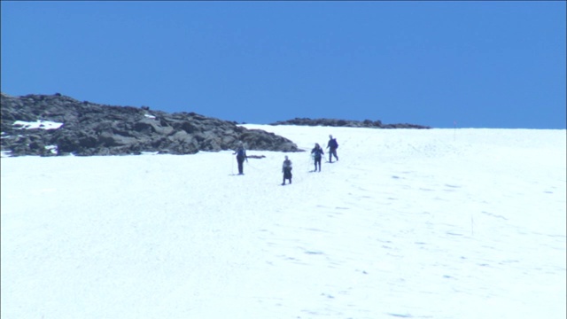 一队徒步旅行者沿着积雪的山坡下山。视频素材