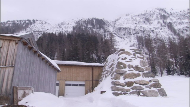 在一座积雪覆盖的山脚下，一道石头控制的栅栏挡住了一条雪崩通道。视频素材