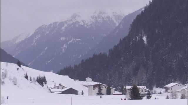 在一个白雪覆盖的山村，行人走在雪崩的小路下面。视频素材