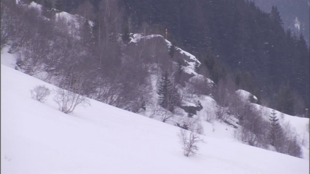 行人和滑雪者在白雪覆盖的山上的雪崩小径下行走。视频素材