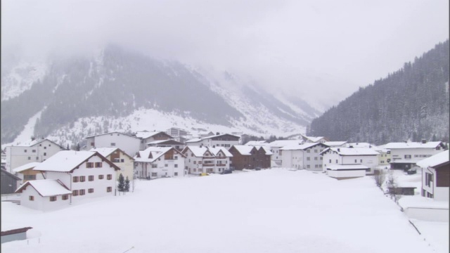 浓雾部分覆盖了一座俯瞰小镇的雪山。视频素材