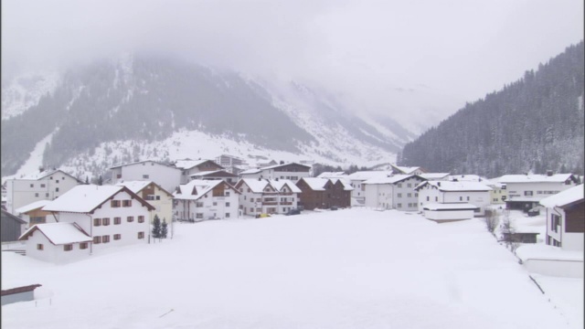 浓雾部分覆盖了一座俯瞰小镇的雪山。视频素材