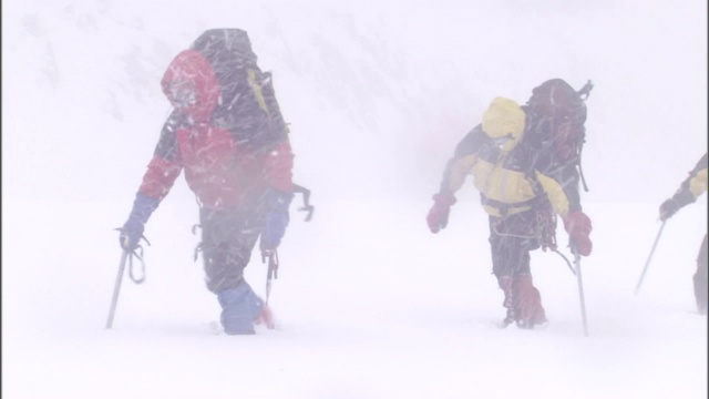 在暴风雪中，穿着冬装背着大背包的徒步旅行者在厚厚的积雪中跋涉。视频素材