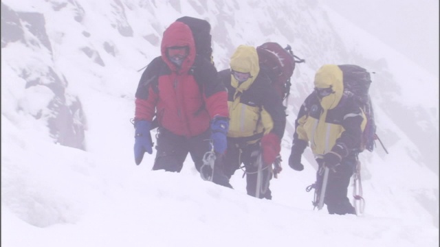 三名背包客在暴风雪肆虐的大雪中艰难前行。视频素材