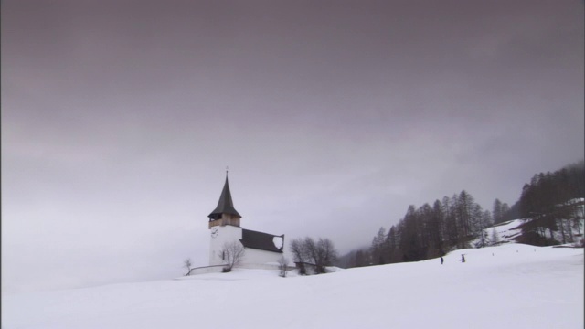 两个人走向雪山上一座风景如画的教堂。视频素材