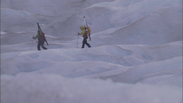 两个滑雪者背着滑雪板爬上一座雪山。视频素材