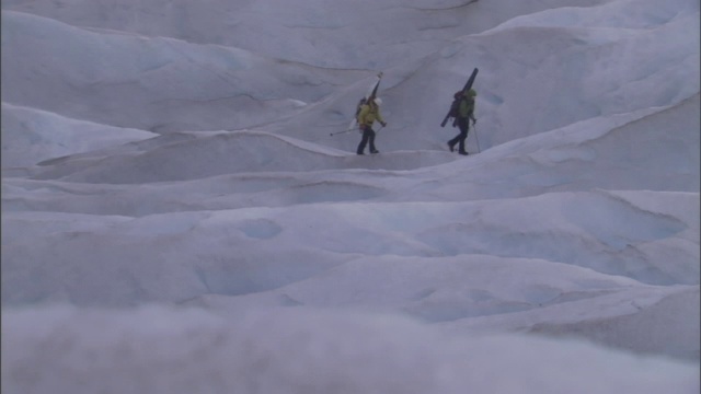 两个滑雪者扛着滑雪板从雪山上滑下来。视频素材