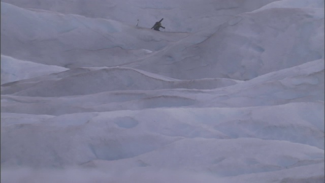 两个徒步旅行者在一座山上的雪堆周围散步。视频素材