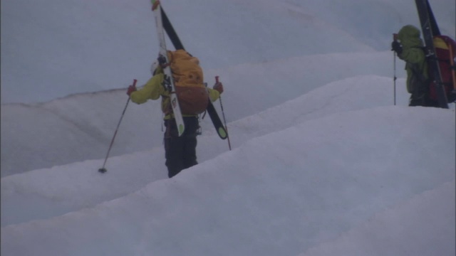 两个人用杆子、背着背包和滑雪板在冰川上徒步旅行。视频素材