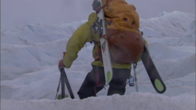 两个人用杆子、背着背包和滑雪板在冰川上徒步旅行。视频素材