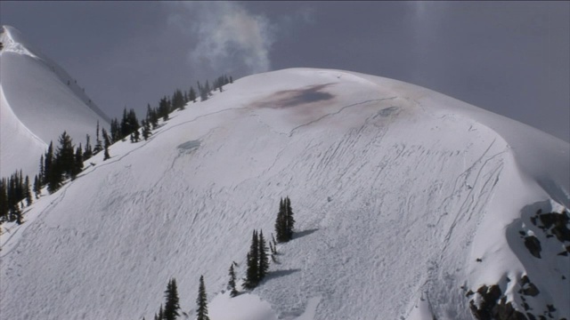 爆炸在陡峭的山腰造成雪崩。视频素材