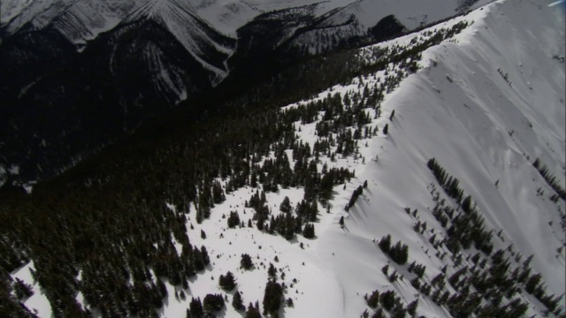 航拍显示了陡峭的积雪和树木覆盖的山脊。视频素材