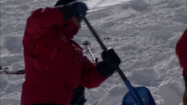 事故模拟小组成员用铲子挖出一条雪崩路径。视频素材