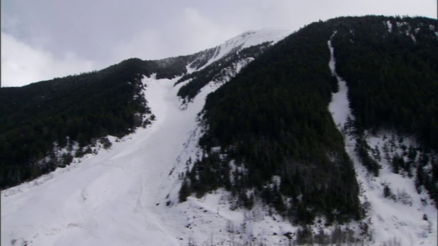 白雪覆盖的山坡穿过一座树木茂密的山。视频素材