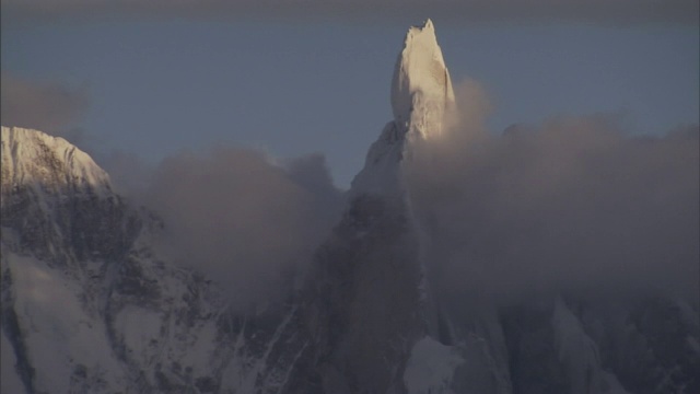 一座白雪皑皑的山峰耸立在厚厚的灰色云层之上。视频素材