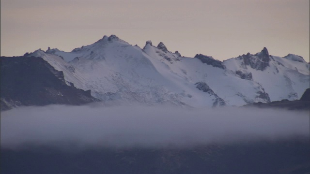 一层白云在白雪覆盖的山顶下飘动。视频素材