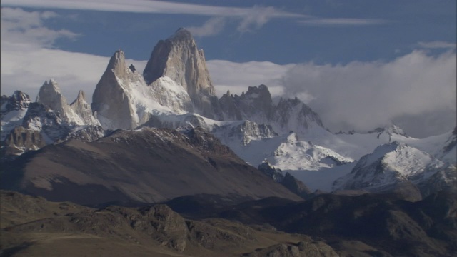 参差不齐的白雪覆盖的山峰映衬着多云的蓝天。视频素材