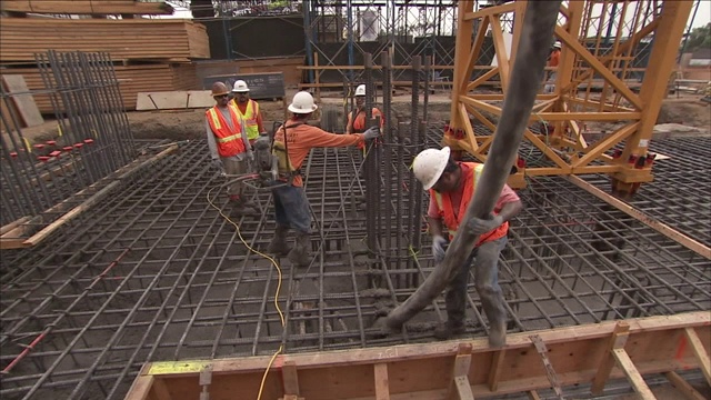 建筑工人引导一根软管将混凝土输送到钢筋基础上。视频素材