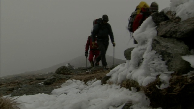 三名徒步旅行者沿着一条雪道走，暴风雪在他们周围肆虐。视频素材