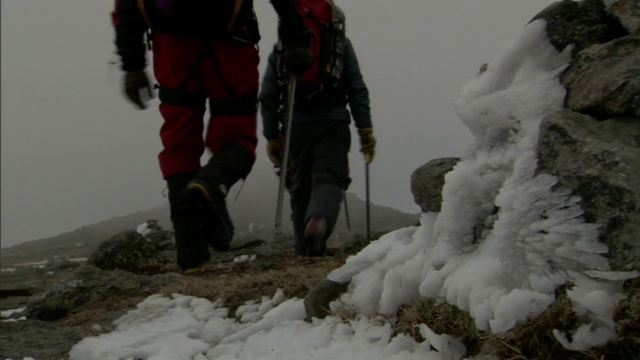 三名背包客使用滑雪杖爬山，这时他们周围刮起了暴风雪。视频素材