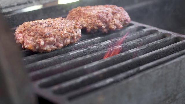 厨师把做汉堡的肉放在烤架上。多汁的肉是用大火煮的。大量的烟雾。烤架上的三个馅饼。视频素材