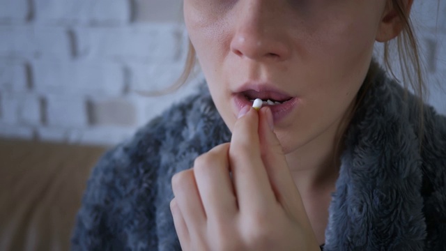 一个年轻生病的白人妇女坐在家里的沙发上吃药的特写。药片在桌子上。悲伤的流感生病的成年人感冒生病的人生病病毒过敏肖像慢动作视频素材