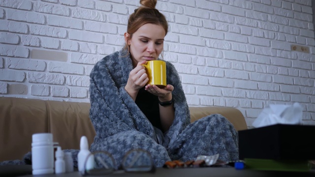 生病的漂亮女人感冒了，喝着柠檬热茶坐在家里的沙发在冬天。流感病成人感冒病人病病毒肖像慢动作药丸视频素材