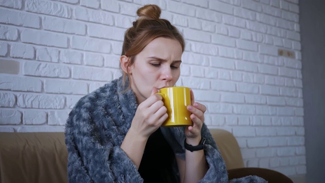 生病的漂亮女人感冒了，喝着柠檬热茶坐在家里的沙发在冬天。流感病成人感冒病人病病毒肖像慢动作药丸视频素材